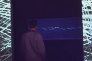 Inside the dark installation, a visitor seen from behind, facing a projection of the word cloud, lit mesh on the walls either side