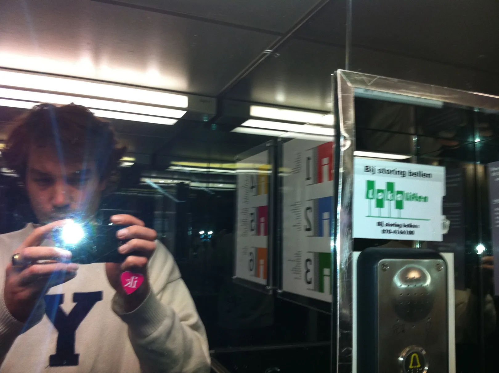 A mirror shot in a lift, the flash firing from the phone, a pink heart sticker on the hand holding it