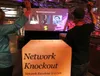 Two players, seen from behind, throwing balls at a projected quiz question with three avatars, the lit Network Knockout crate in front of them