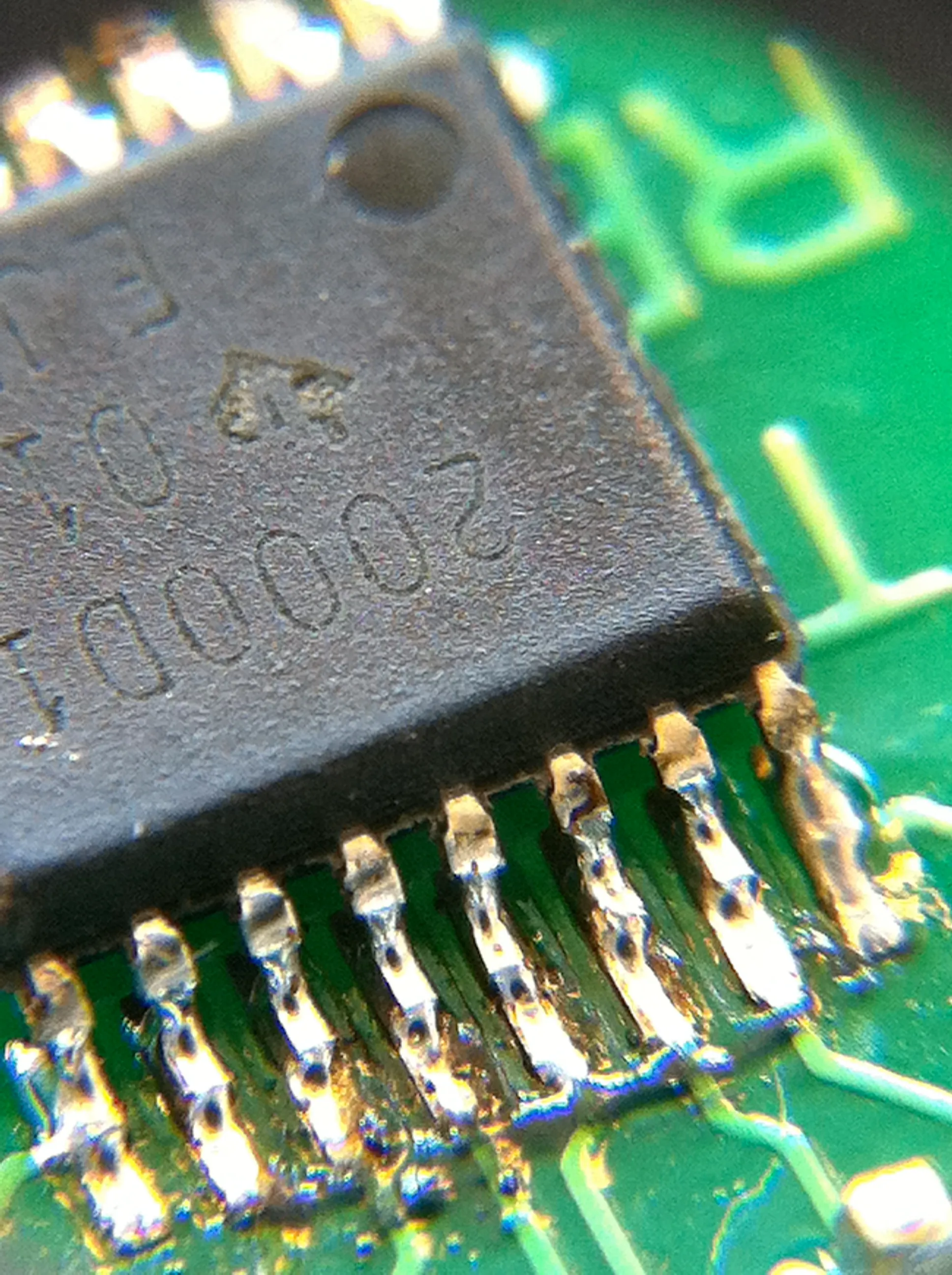 Macro shot of a tiny surface-mount amplifier chip hand-soldered onto a green breakout board