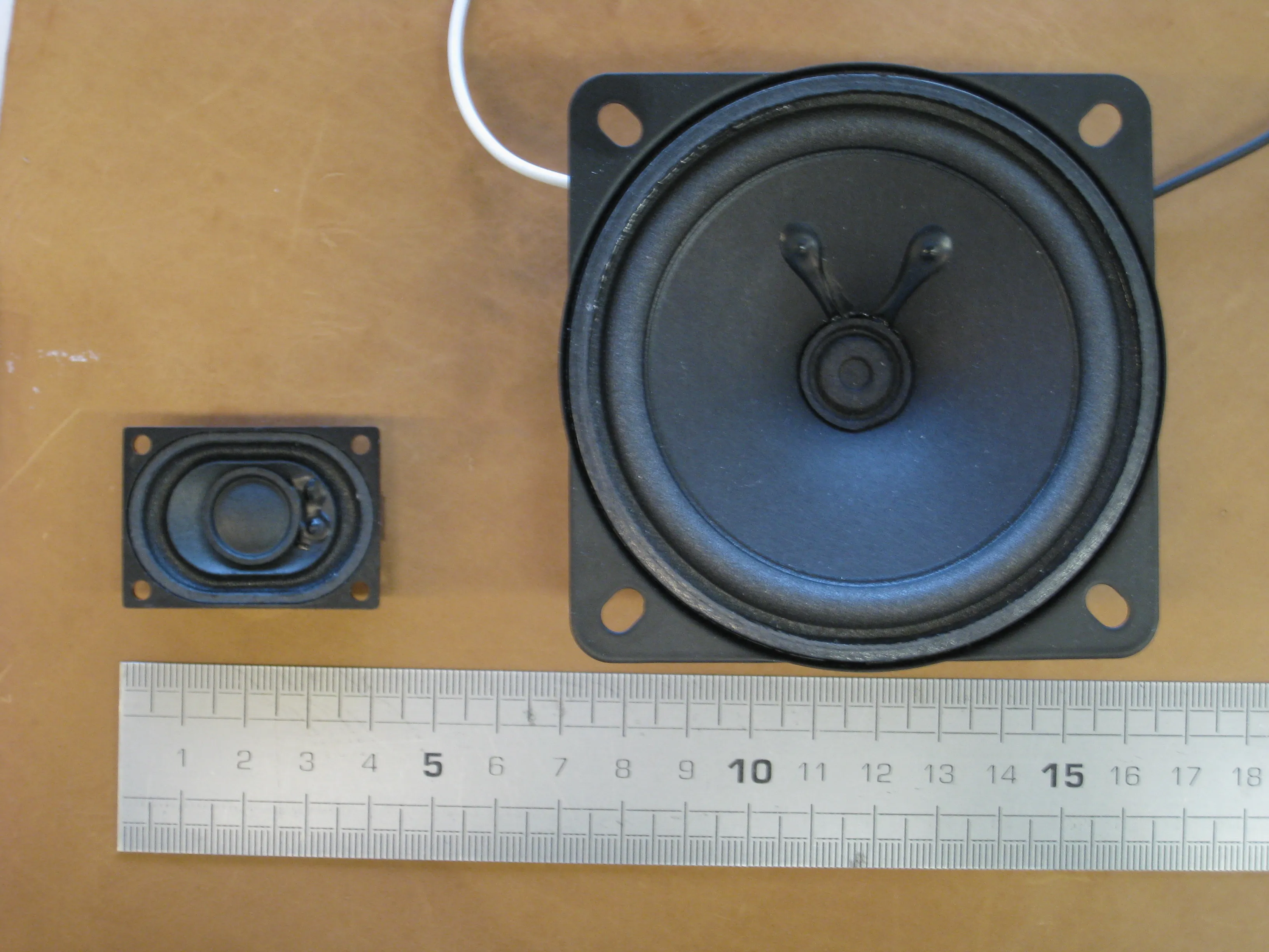 A small oval speaker next to a larger round one, with a ruler for scale