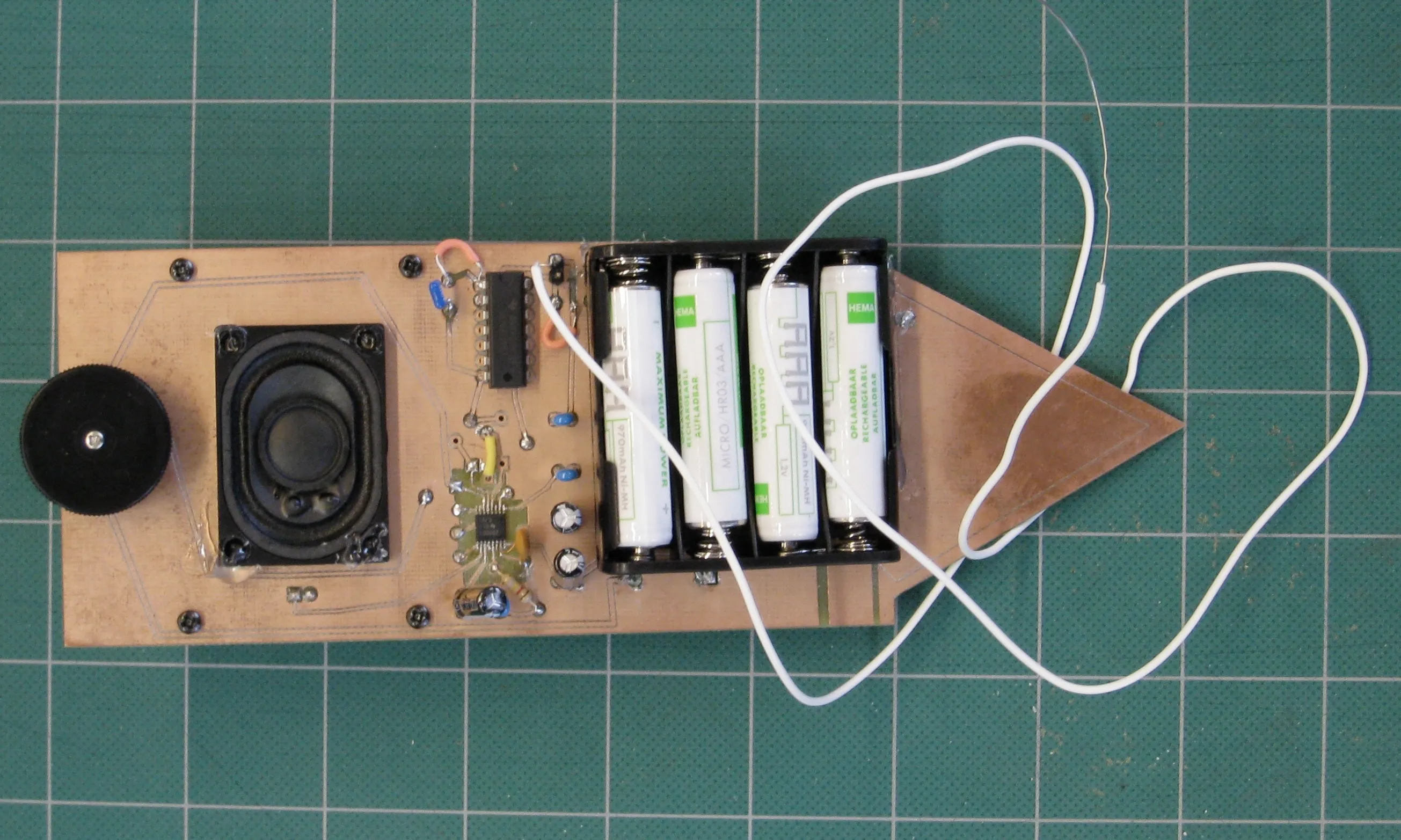 The finished board on a cutting mat, with four batteries in the holder and a long white wire looping off the tip