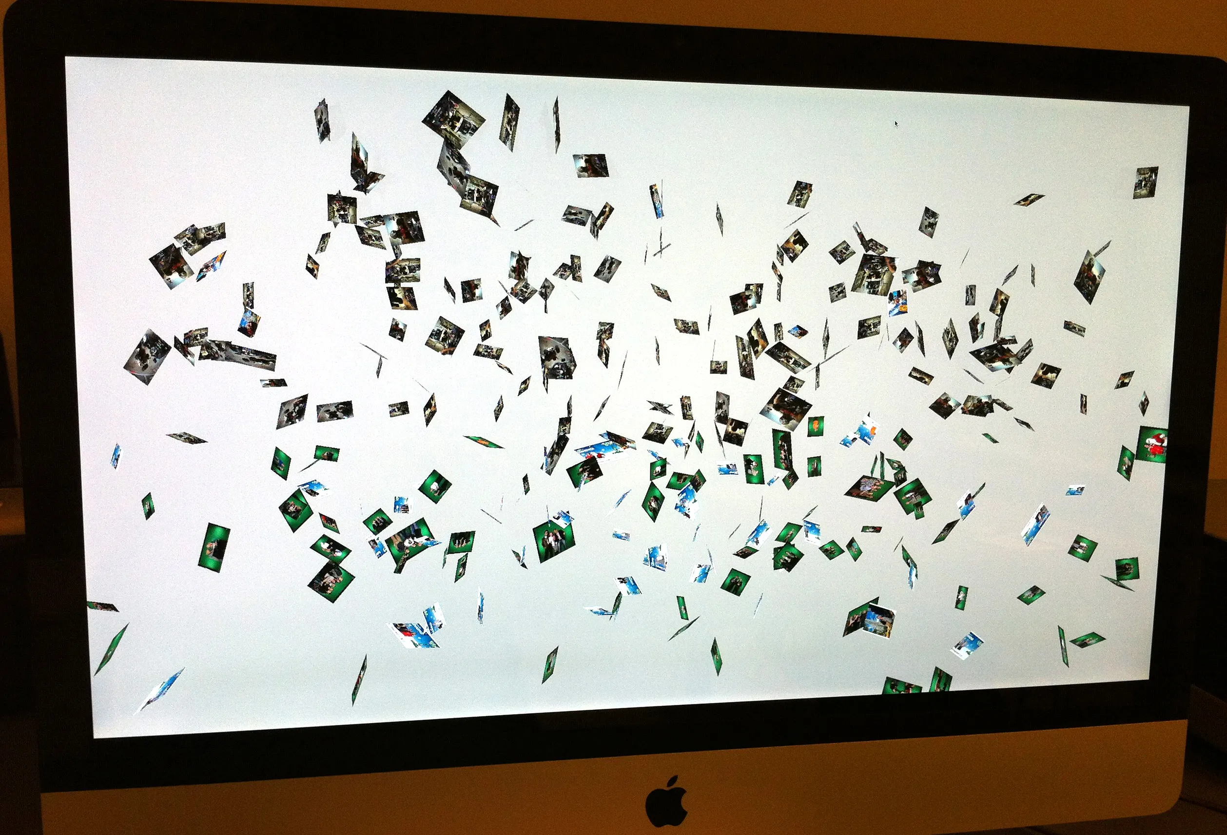 An iMac showing the animation: hundreds of small portrait photos tumbling across a white screen