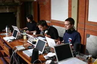 Workshop participants with headphones at laptops along a long table in an old room of the Waag