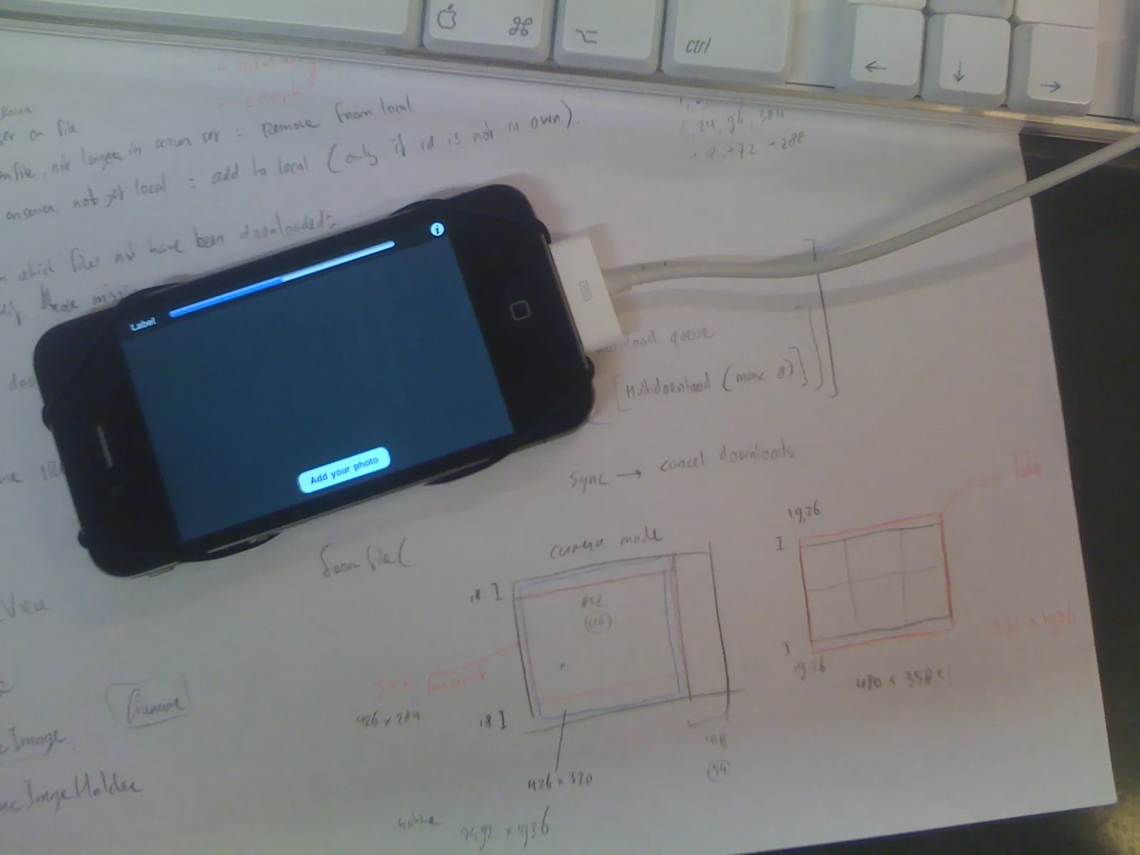 An early build on an iPhone 4, lying on handwritten notes about syncing and sketches of the camera-mode layout