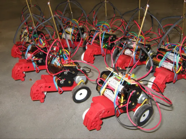 A group of finished robots close together, each with AA batteries, a small circuit board with LEDs and a cage of wire