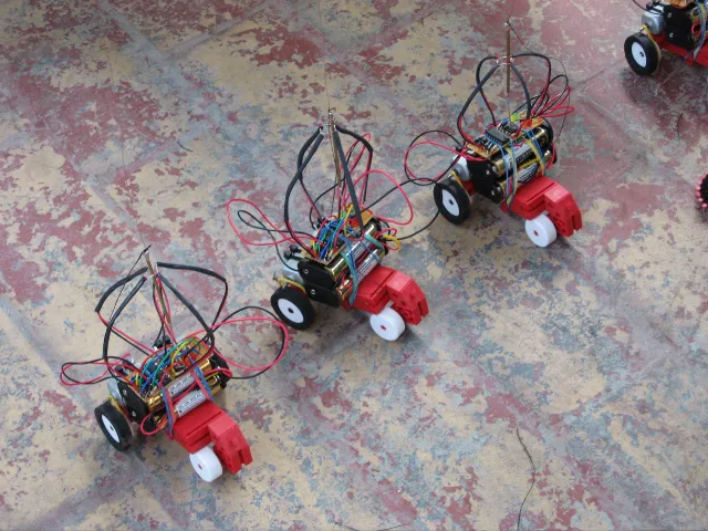 Robots driving in a loose line over a worn, red painted floor, seen from above