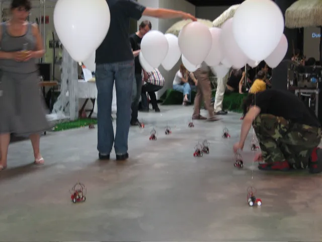 Visitors among the robots, one crouching down to a robot, another reaching out to a balloon