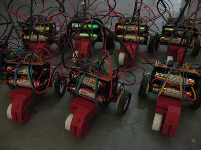 Close-up of a row of robots in low light: batteries, wiring and red chassis
